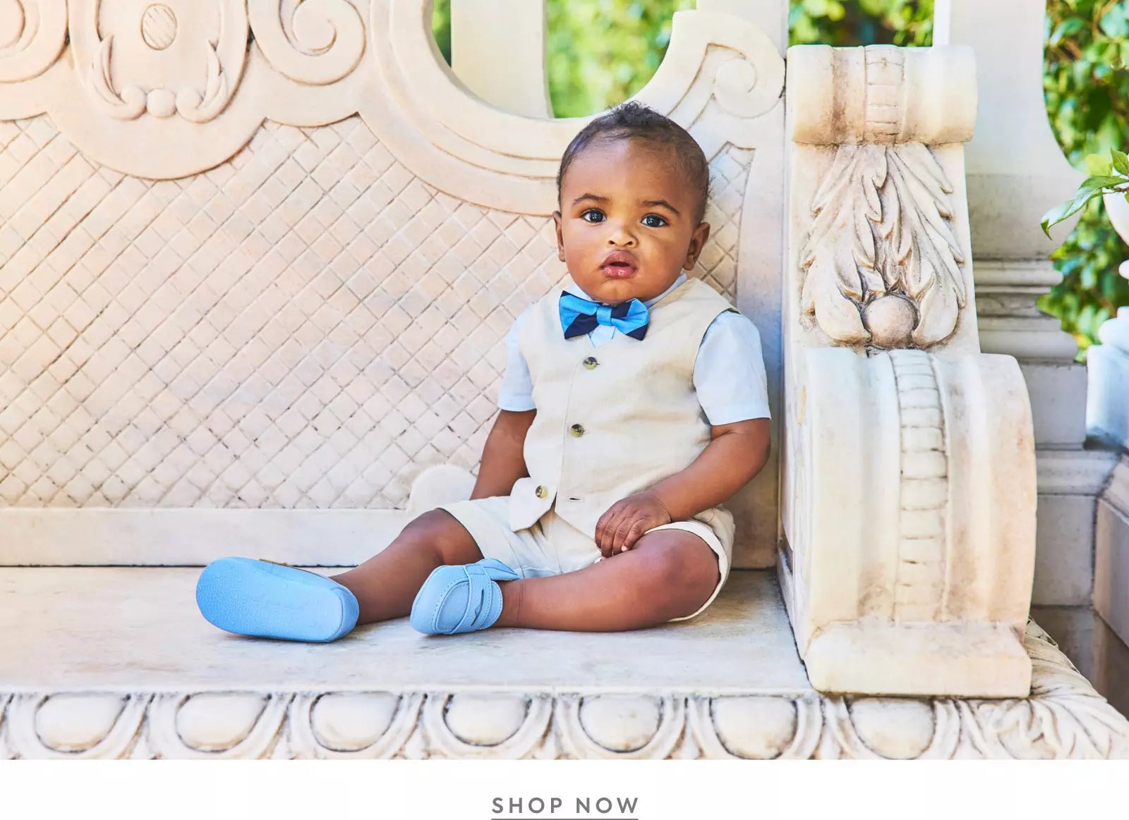 Child in formal attire sitting on an ornate bench with 'Shop Now' text overlay.
